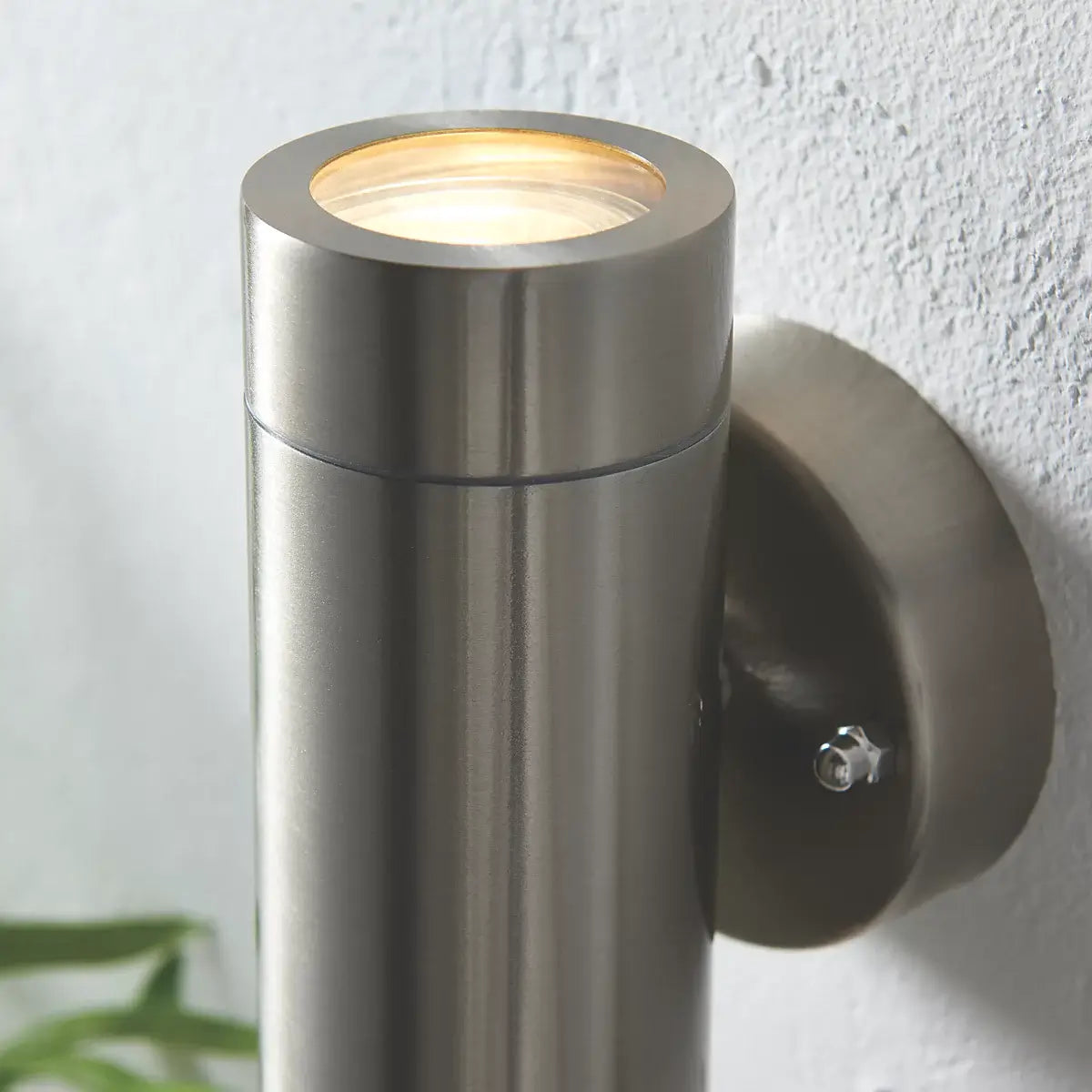 The image shows a sleek, cylindrical, silver outdoor wall light with a modern, minimalist design. It features an up-and-down lighting configuration, mounted on a round base.