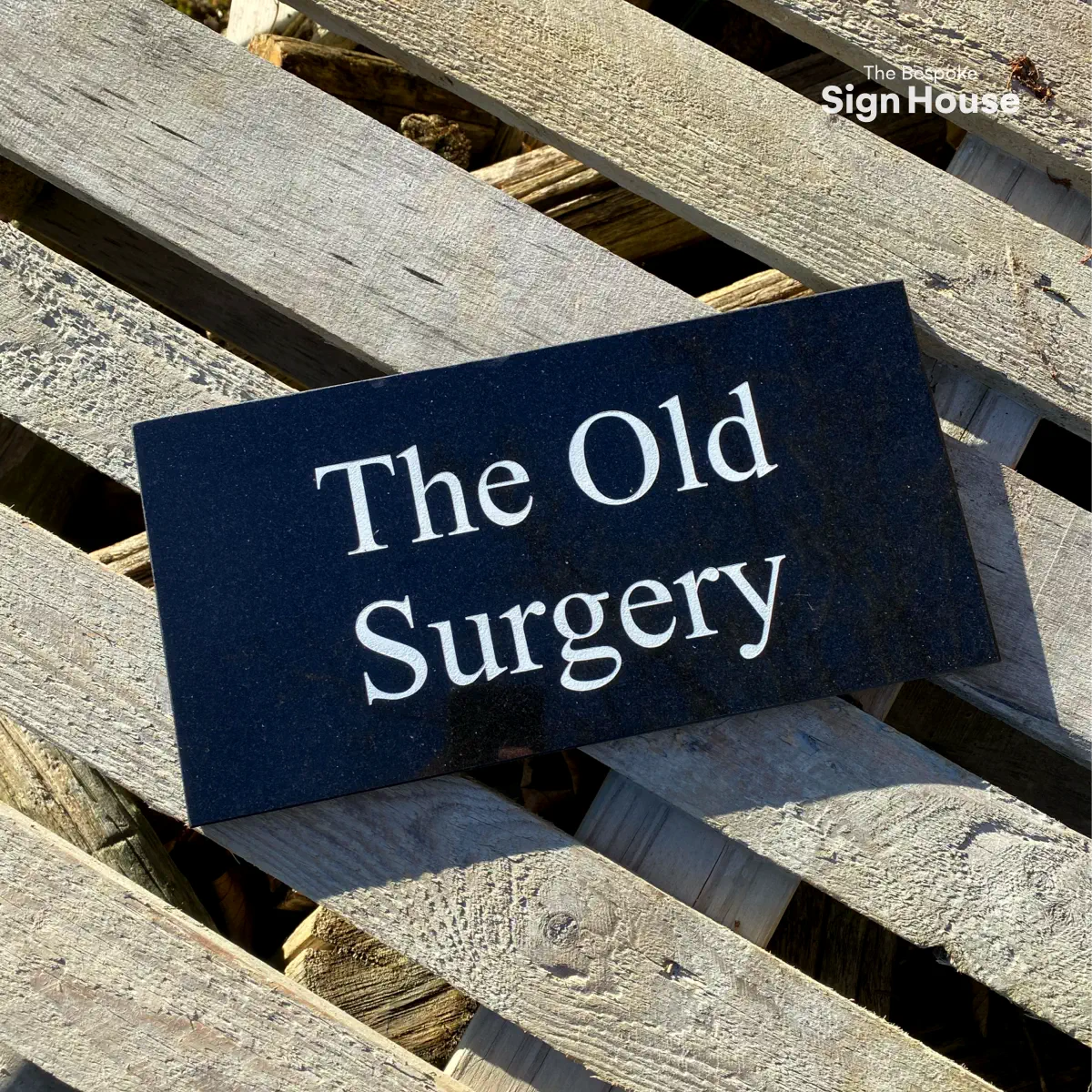 a rectangular granite house sign with a customers house address engraved and painted white on it. The signs reads The Old Surgery