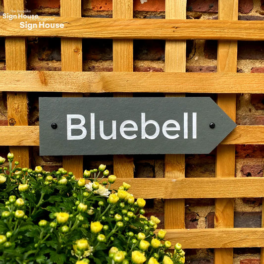 a slate sign on a wooden trellis with the wording Bluebell engraved into the slate surface and painted white