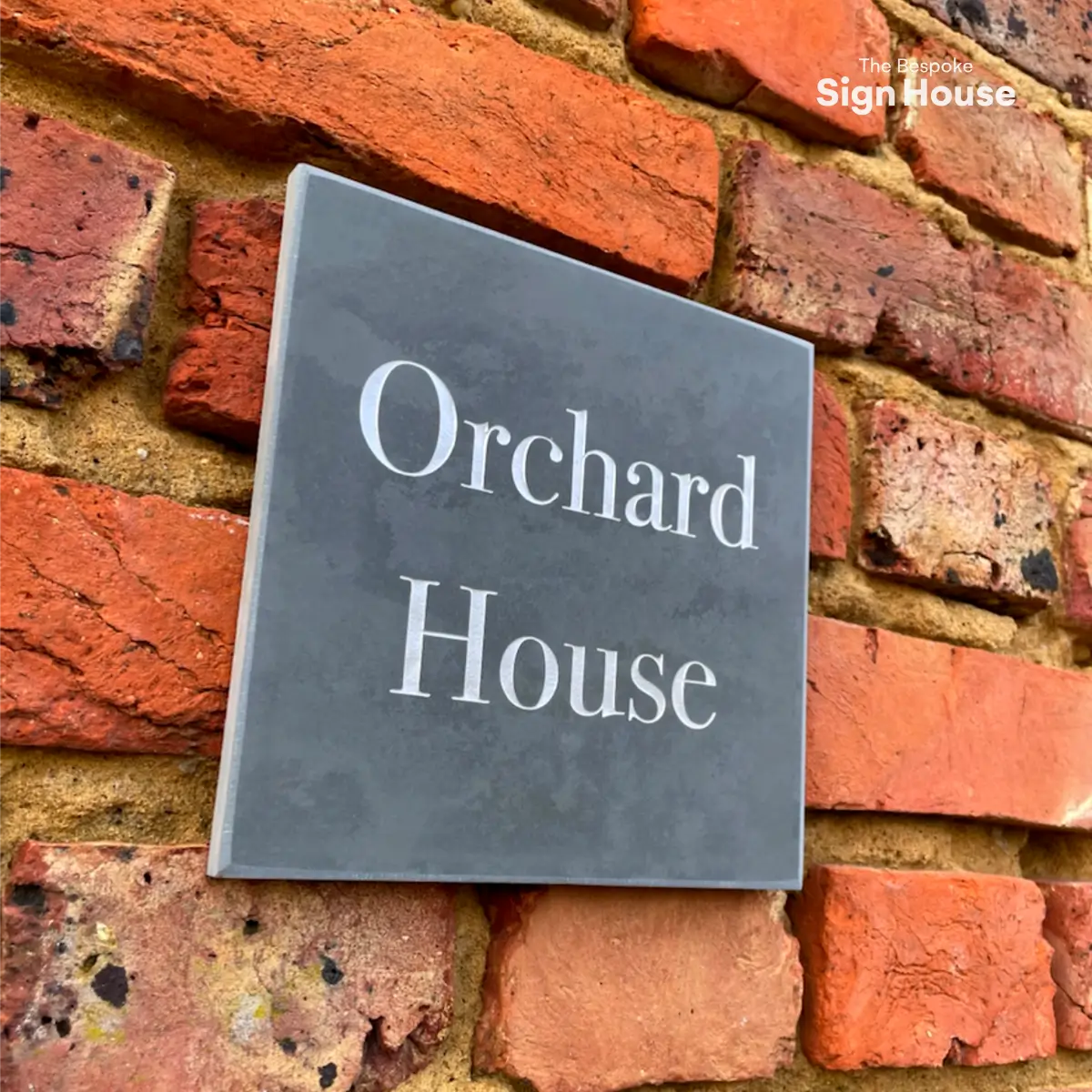 Custom slate house sign mounted on a red brick wall with the text ‘Orchard House’ engraved in white.