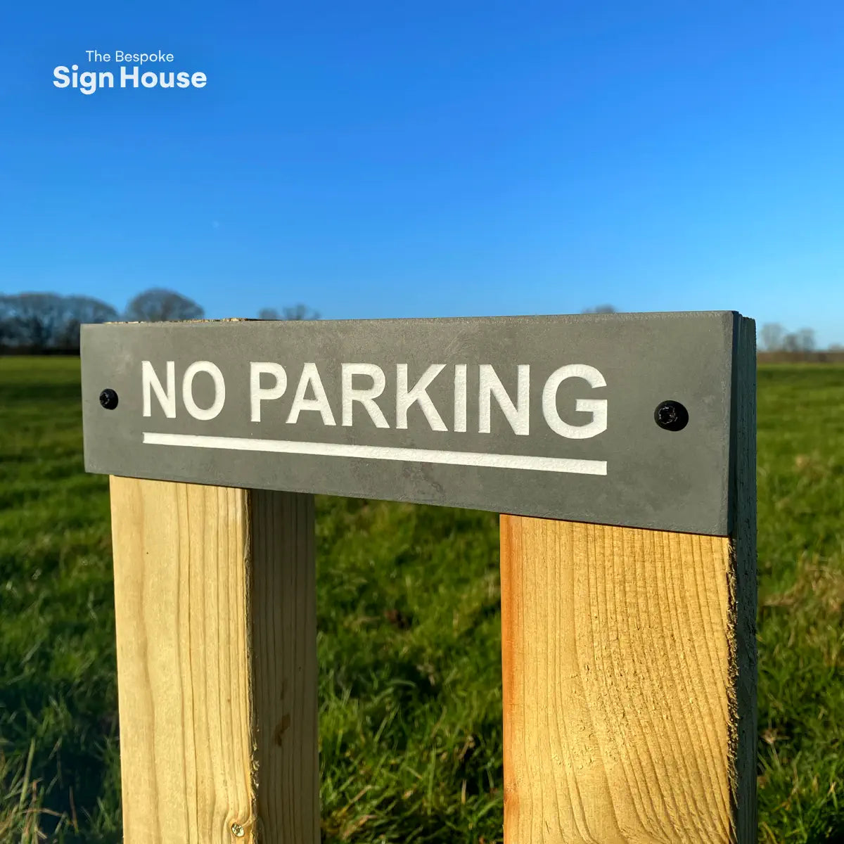 a posted slate sign that says no parking. the text is engraved into the slate sign and painted white