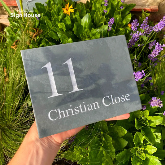 a slate house sign with a number and street name engraved into it and painted white. The text and number is aligned to the left. The sign reads 11 Christian Close