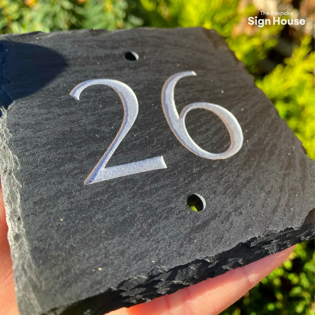 a small grey slate door number sign with 26 engraved and painted into it in silver