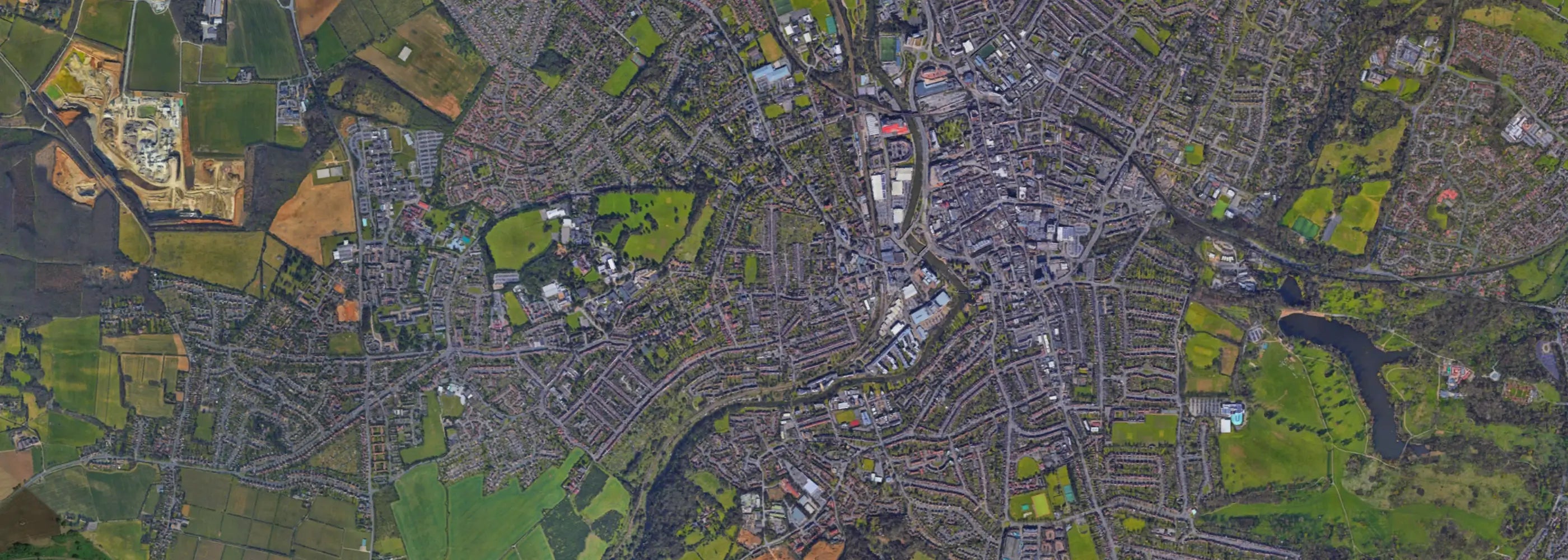 Aerial view of a densely populated town surrounded by fields, showing a mix of residential areas, green spaces, and industrial zones